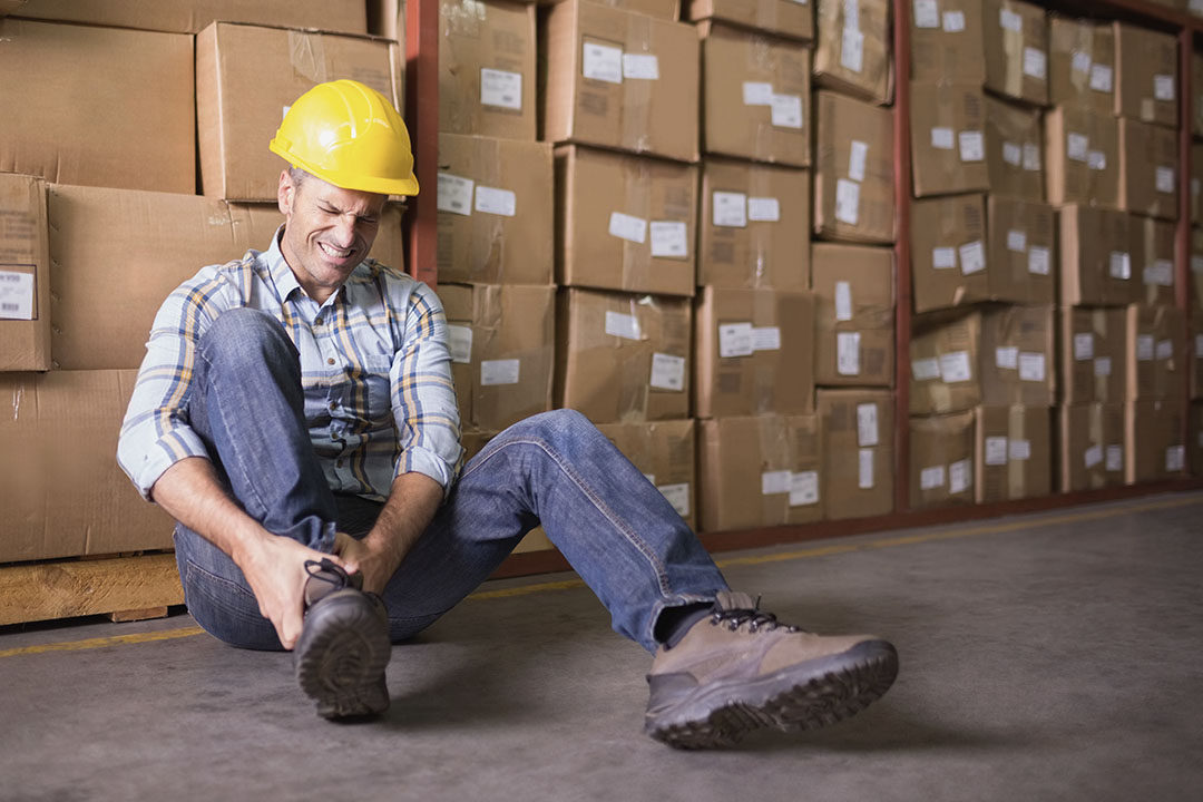 male worker sitting with sprained ankle in warehouse