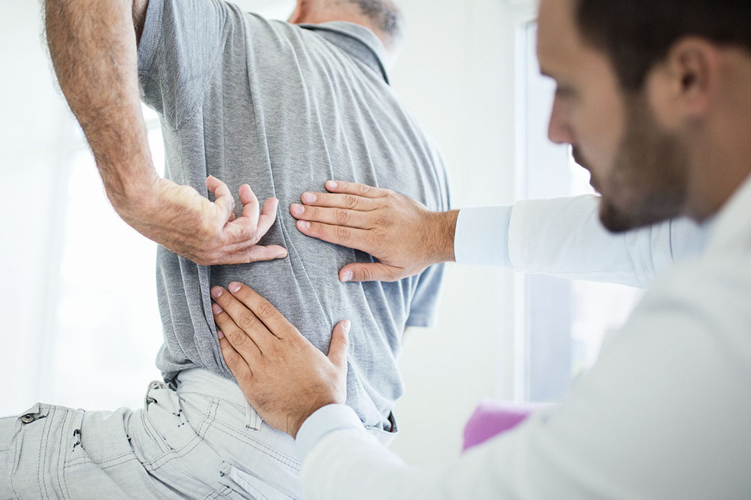 older man pointing to back injury doctor examining him, in need of neck and back injury attorneys
