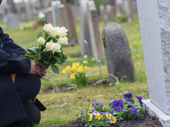 woman with flowers kneeling by grave at cemetery