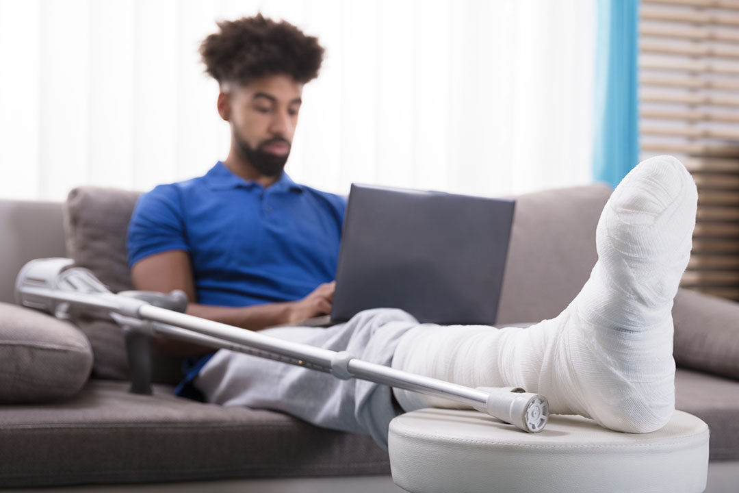 young man with broken leg sitting on couch using laptop
