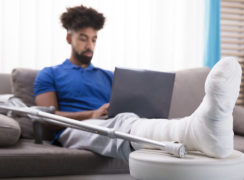 young man with broken leg sitting on couch using laptop to find a St. Louis personal injury lawyer.