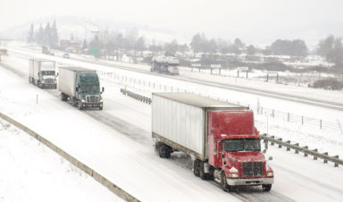 Three semi-trucks drive on snowy roads.