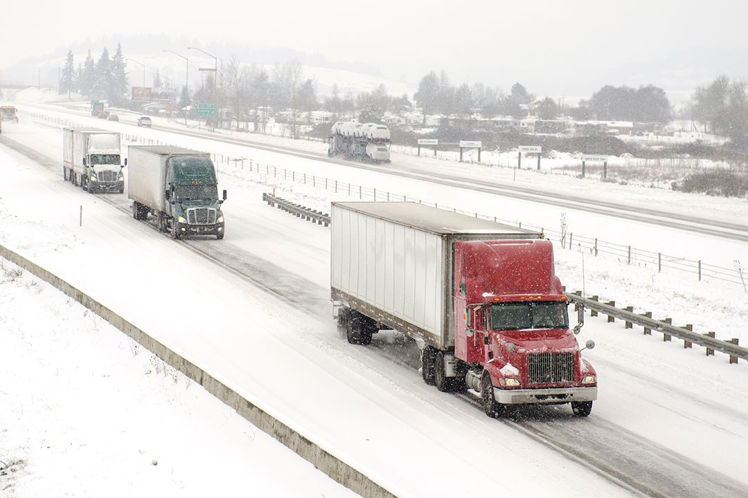 Three semi-trucks drive on snowy roads.