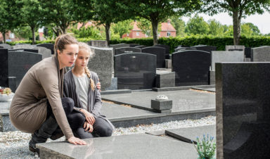 A younger woman and older woman embrace by a grave of a family member who died a wrongful death.
