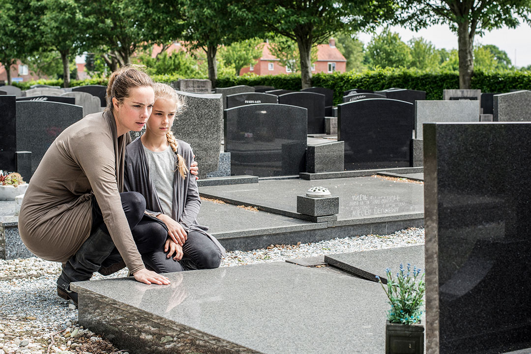 A younger woman and older woman embrace by a grave of a family member who died a wrongful death.