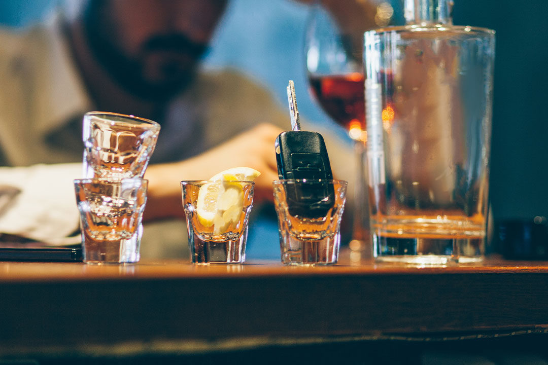 A man sits at a bar with numerous empty shot glasses as a representation of dram shop liability in a drunken driving crash case.