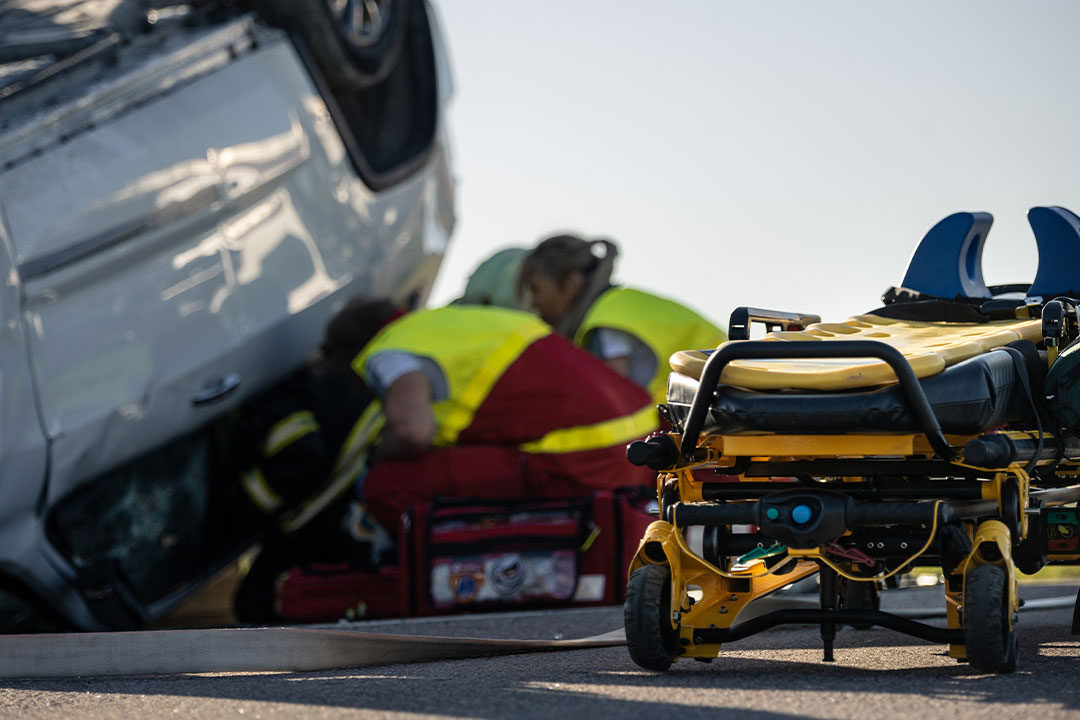 An EMT helps a victim after a serious injury from a car accident, with a stretcher nearby.