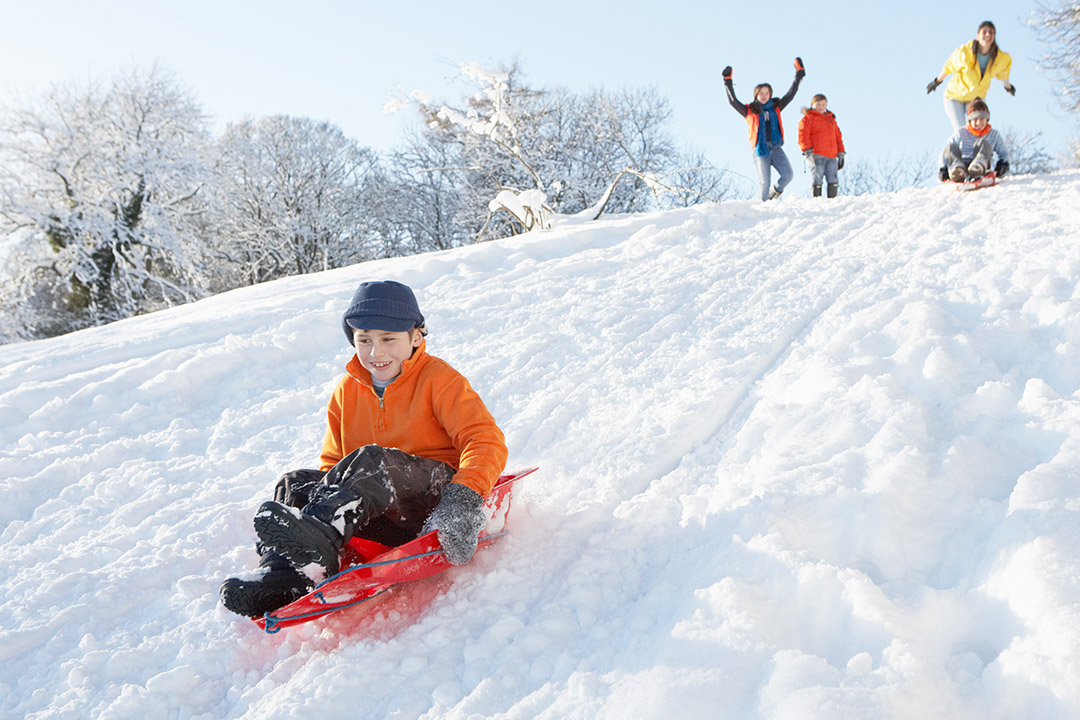 Children engaging in outdoor winter activities, with one child sledding down a snowy hill.