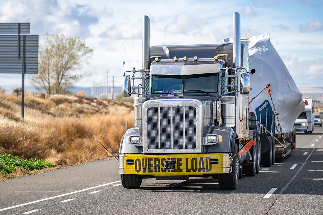 A semi truck driver follows truck driving rules by having a large yellow "Oversized Load" sign on the front of his vehicle.