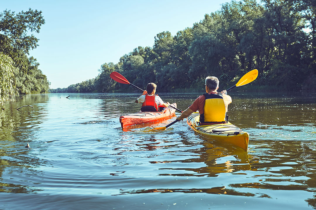 Two people are on a float trip, paddling down a river in kayaks.