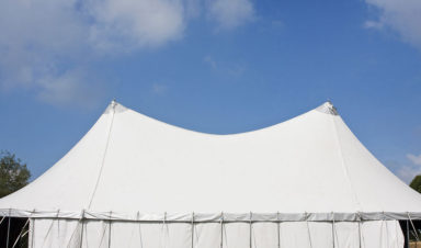 A large white tent is erected on grassy land, with a blue sky in the background, prior to a collapsed tent accident