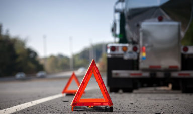 A semi truck's roadside parking is indicated by the placement of red cones on the side of the highway behind the truck.