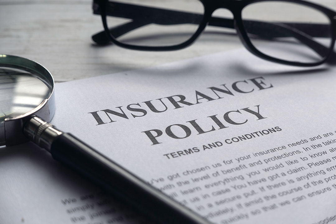A pair of black glasses and a magnifying glass rest on top of an insurance policy terms and conditions document.