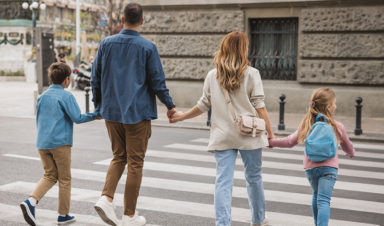 A heteronormative family of four crosses the street, holding hands and using the crosswalk to avoid a pedestrian crash.